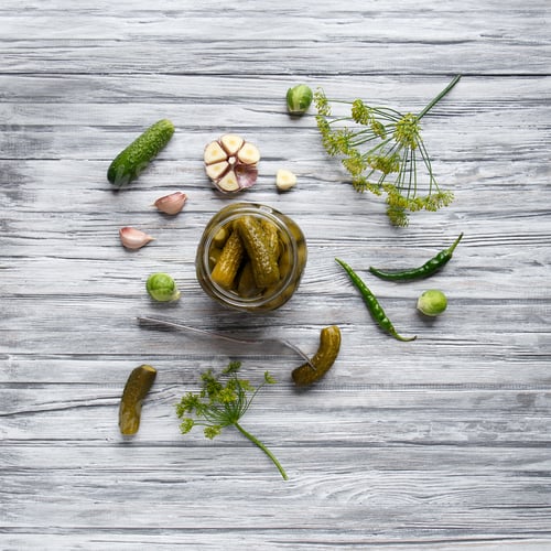 Preview: Open jar with pickled cucumbers and cucumber on a fork on a wooden background, top view, copy space.