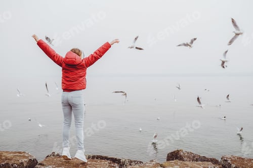 Preview: Back view of young teen girl with hands raised up near the sea looking at flying seagulls. Dreams