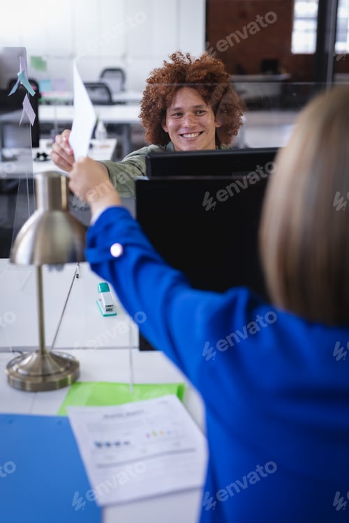 Preview: Diverse male and female colleagues in front of computers with sneeze shield hand document