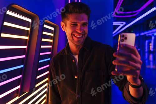 Preview: Young bristle man smiling while taking selfie on mobile phone