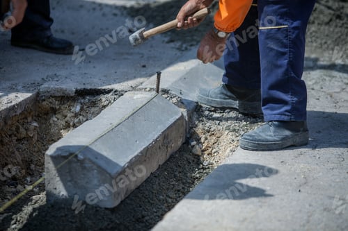 Preview: Worker with an orange uniform installing a sidewalk with a big hammer