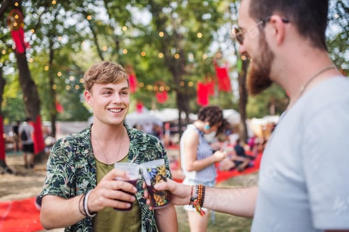 Preview: Young friends with drinks at summer festival, clinking glasses