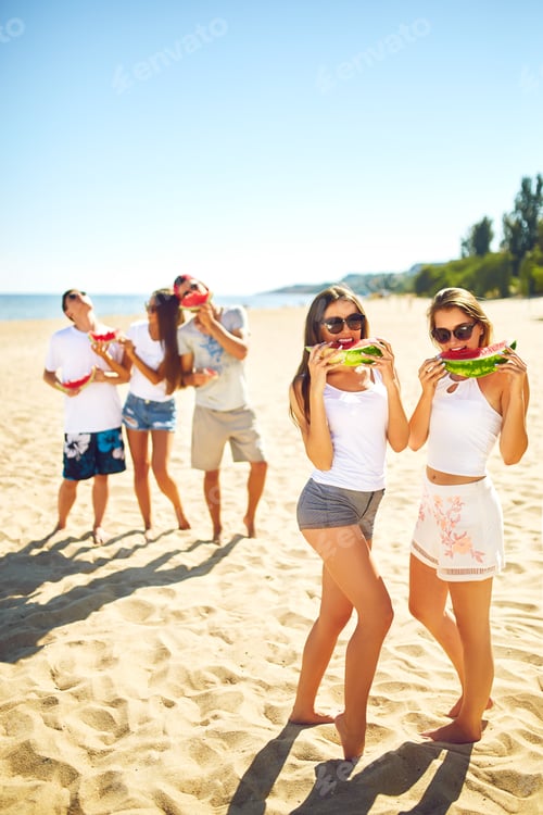 Preview: Group of friends having fun eating watermelon on beach. Excellent sunny weather. Super mood. Summer.