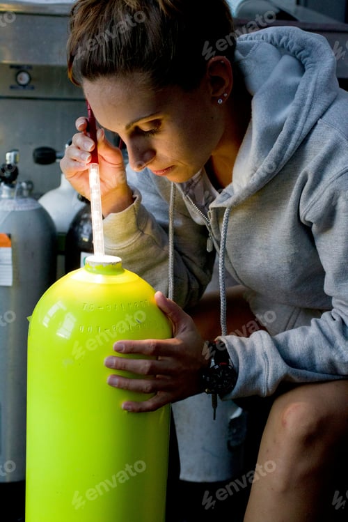 Preview: Scientist in a hooded sweater intently measuring liquid from a large yellow container