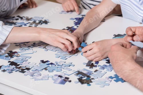 Preview: Cropped image family playing with puzzle on table at home together