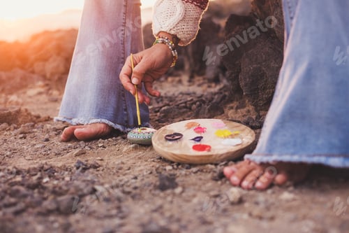 Preview: feet of woman barefoot on the ground while she paints a mandala