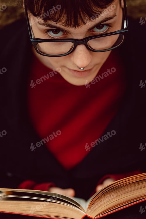 Preview: Young woman reading book on bench in park