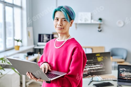 Preview: Asian young man looking at camera in office and holding laptop