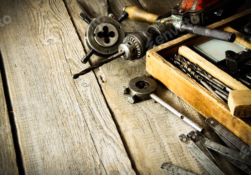 Preview: Old drill, a box with drills, pliers and ruler on wooden background.