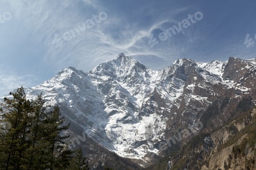 Preview: Majestic snow capped mountain peaks towering over the forest on a sunny day with blue skies