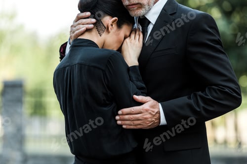 Preview: cropped view of sad elderly man embracing woman on funeral