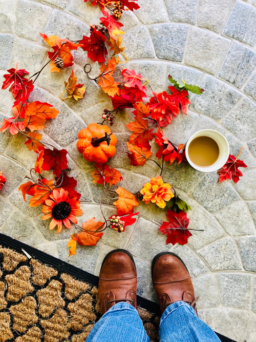 Preview: Autumn flat lay, overhead shot of fall leaves and blooms on the ground, and a woman’s feet.