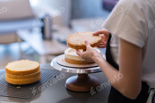 Preview: Confectioner in black apron connecting organic cake layers with fresh white cream