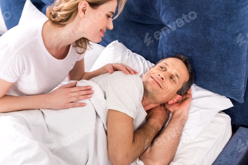 Preview: smiling couple looking at each other while lying in bed at home