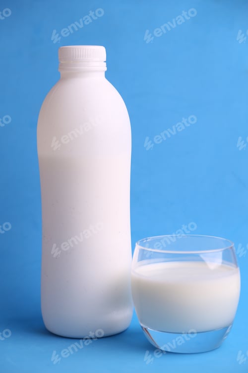 Preview: Vertical shot of a white bottle and a glass full of milk in front of a blue background
