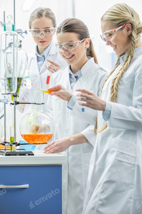 Preview: Three young smiling female scientists making experiment in chemical lab
