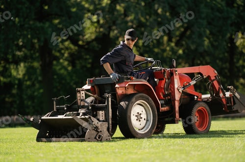 Preview: Man is with utility tractor with grass cutter and aerator equipment on the field