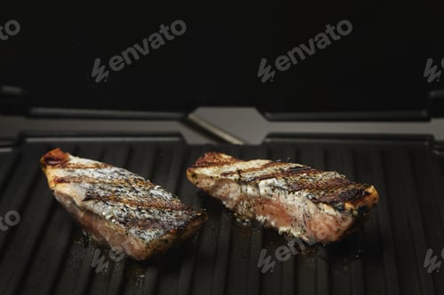 Preview: two pieces of salmon roasted close up on home electronic grill plate tasty diet fish meal