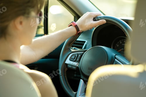 Preview: Close up view of woman holding steering wheel driving a car on city street on sunny day