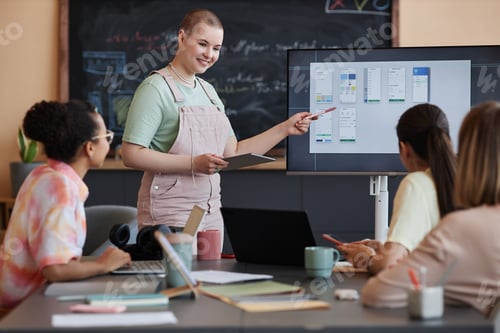 Preview: Smiling bald woman pointing at computer screen presenting to all female team