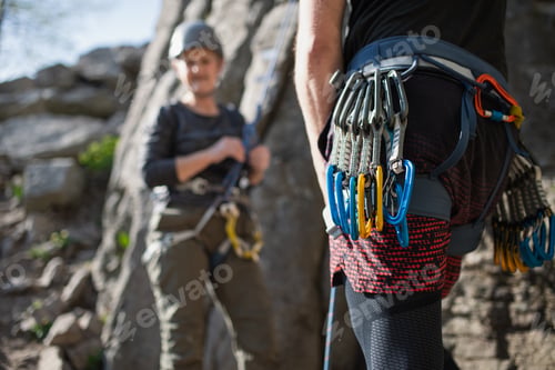 Preview: Instructor with harness and carabiners climbing rocks with seniors outdoors in nature.