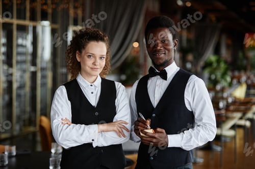 Preview: Two servers wearing classic tuxedo uniform smiling at camera in restaurant
