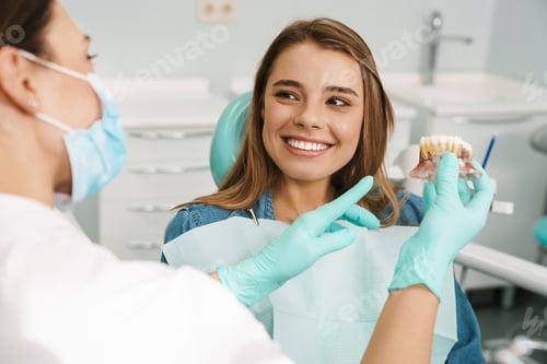 Preview: Dentist woman showing teeth imitation to her smiling patient
