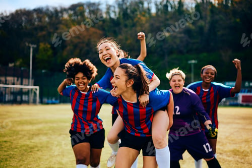 Preview: Excited teammates celebrating victory during women's soccer match on playing field.