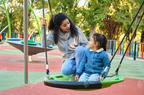 Preview: Latin mother playing with her son on a swing in a park.