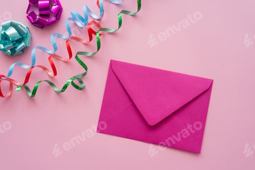 Preview: Top view of envelope near serpentine and gift bows on pink background