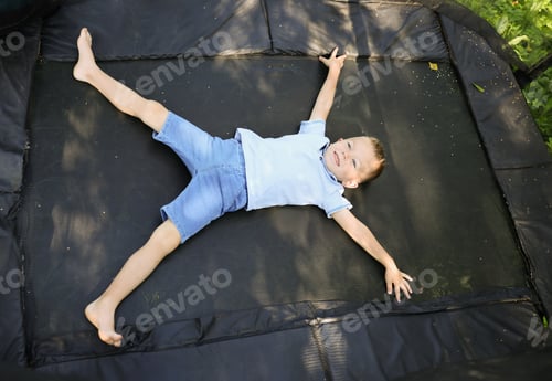 Preview: Happy little boy lying on black trampoline outdoors, above view