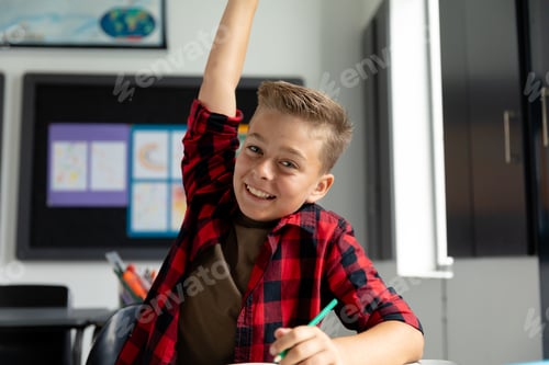 Preview: Eager, smiling caucasian schoolboy sitting at desk raising hand in class