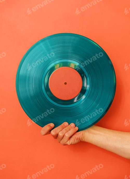 Preview: Man's hand holds blue vinyl record against aorange wall