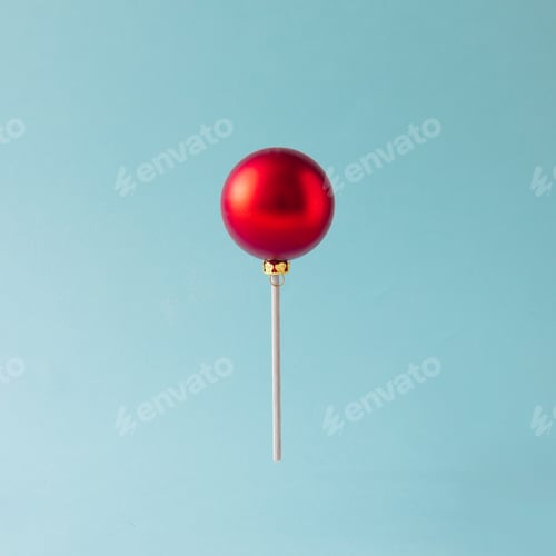 Preview: Lollipop made of red Christmas bauble on blue background. Christmas sweets concept.