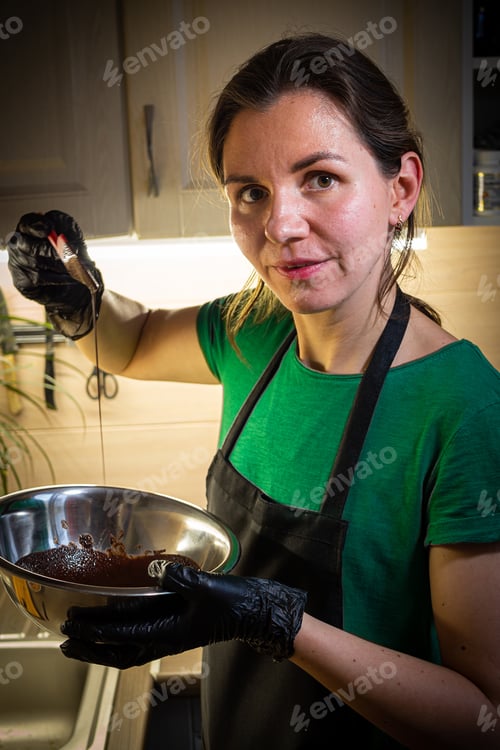 Preview: Woman cooking tasty melted chocolate on table in kitchen.