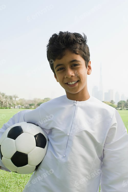 Preview: Young boy smiles holding a soccer ball on a sunny day at the park
