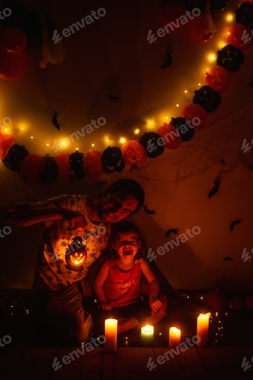 Preview: Father holds pumpkin lantern, daughter is having fun in the dark among candles Halloween decorations