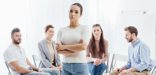 Preview: panoramic shot of woman with arms crossed looking at camera while people sitting during group