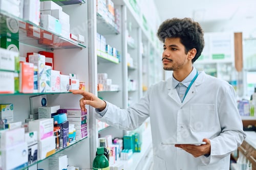 Preview: Young pharmacist going through inventory of medicines on the shelves in drugstore.