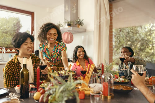 Preview: Happy friends enjoying in conversation and drinking wine during festive dinner at home party