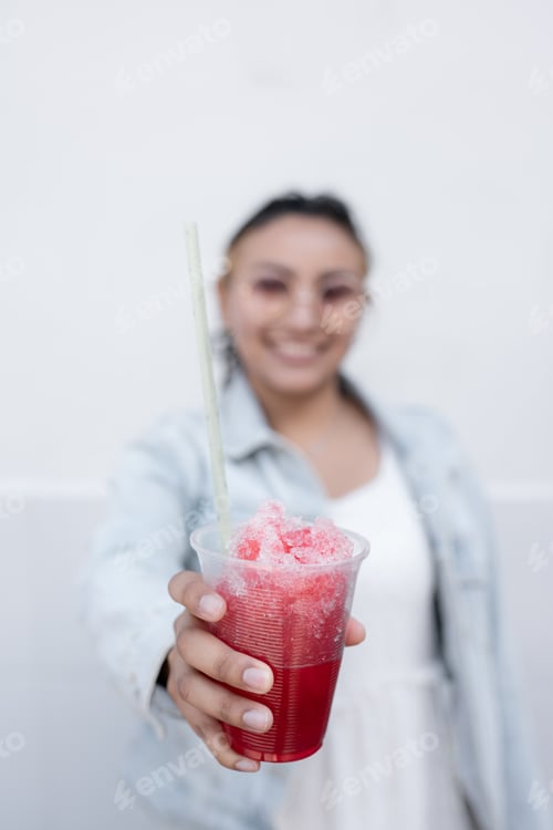 Visualização: Uma jovem hispânica está sorrindo enquanto bebe uma lama de cereja mexicana ao ar livre