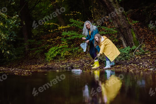 Preview: Small girl with grandmother picking up waste from little lake outoors in forest