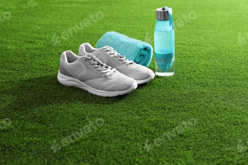 Preview: Bottle of water, sneakers, towel and space for text on artificial grass. Fitness equipment