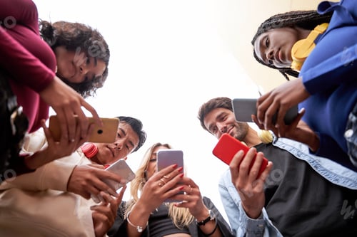 Preview: Multi-ethnic friends using their mobile phones while standing in a circle.