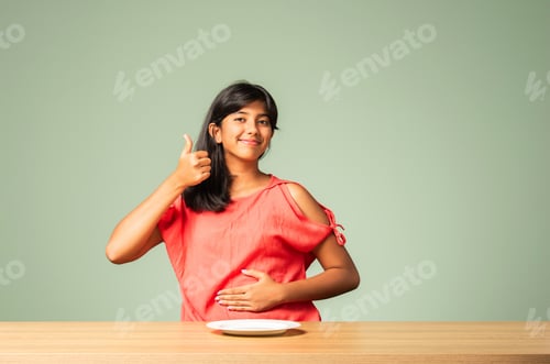 Preview: Asian Indian adorable girl child holding empty ceramic plate with happy emotions, sitting on table