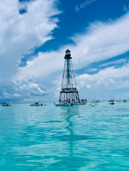 Preview: Lighthouse out in the beautiful blue ocean with white clouds in the sky.