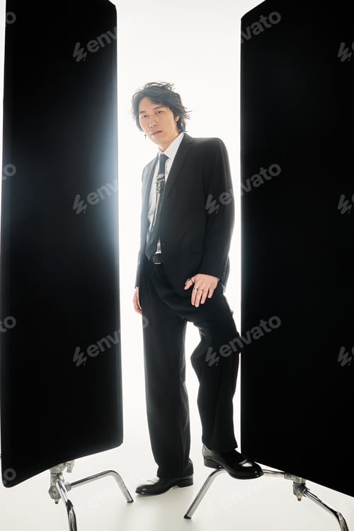 Preview: Stylish young asian man posing confidently in a sleek urban setting under bright studio lights