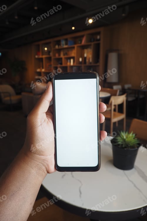 Preview: Person Holding a Smartphone with Blank Screen in Cafe Setting