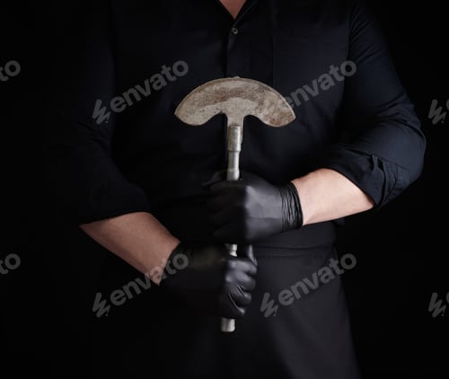 Preview: Man in black clothes, latex gloves holds a vintage metal ax-knife