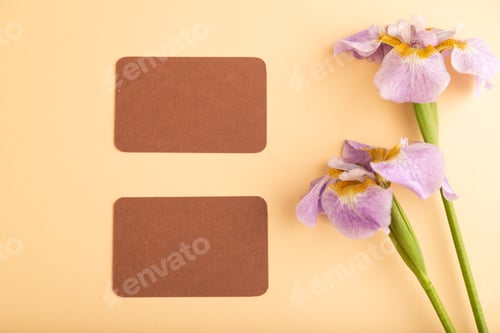 Preview: Brown business card with lilac iris flowers on orange pastel background. top view, copy space.